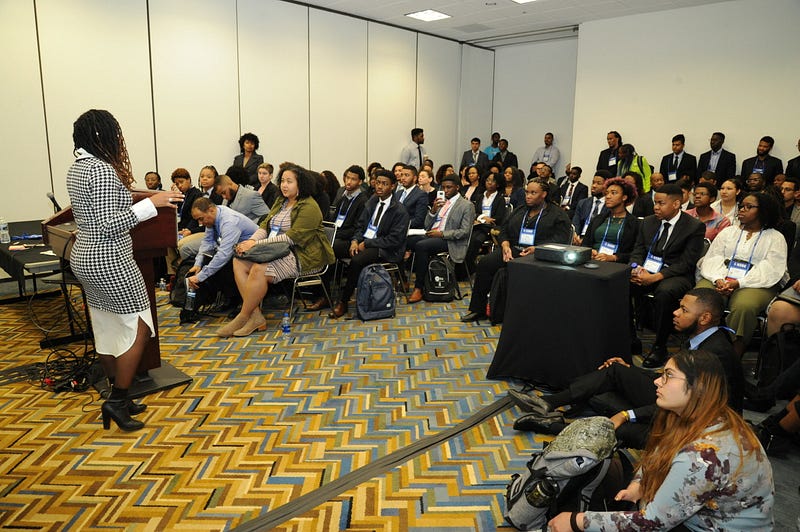 Dr. Grayson standing in the front of a room filled to capacity with Black engineers.