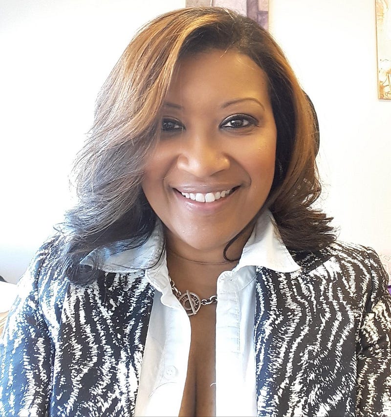 In this headshot photo, Sharron wears a white blouse under a zebra print blazer and smiles at the camera