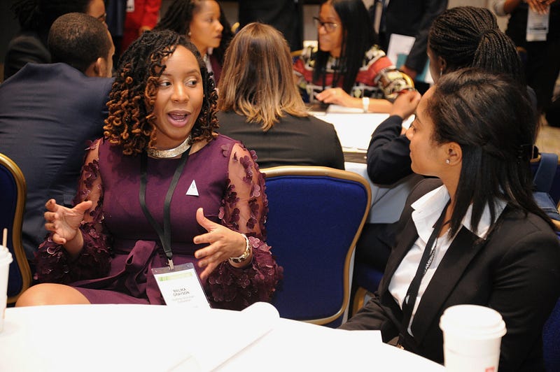 Malika and her conversation partner sitting at a conference table talking.