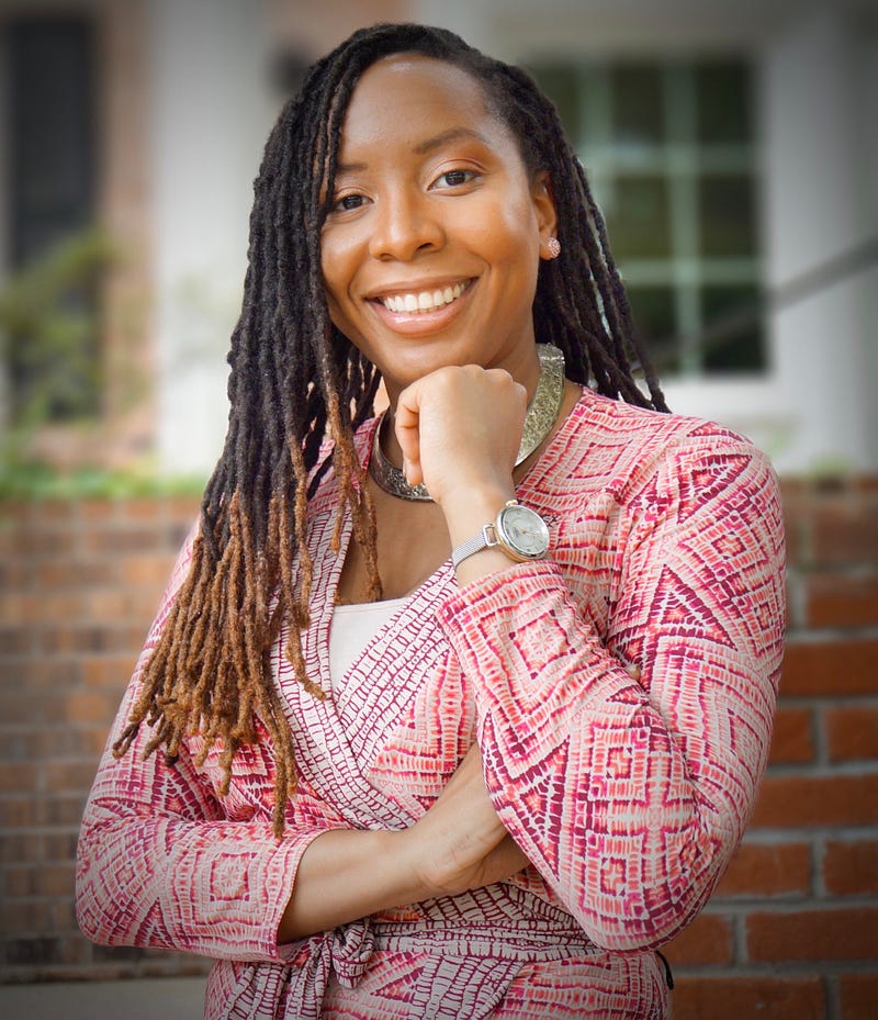 Dr. Malika Grayson standing outside smiling in a multicolored wrap top.