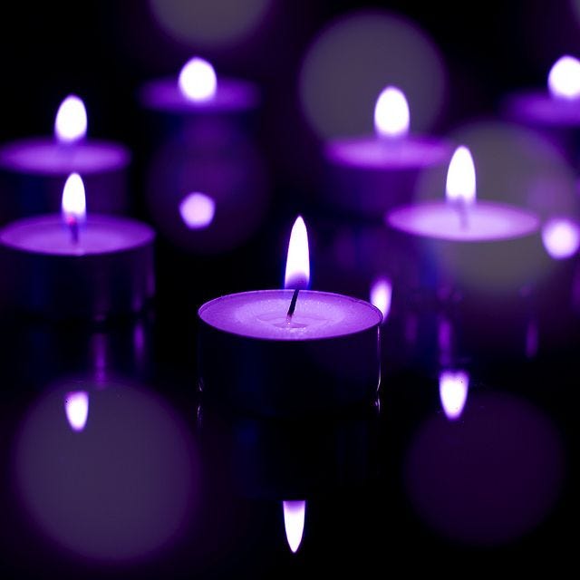 A closeup image of a collection of lit purple candles.