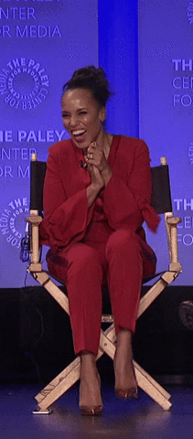 A gif of Kerry Washington shaking in excitement while sitting on stage in a red pantsuit.