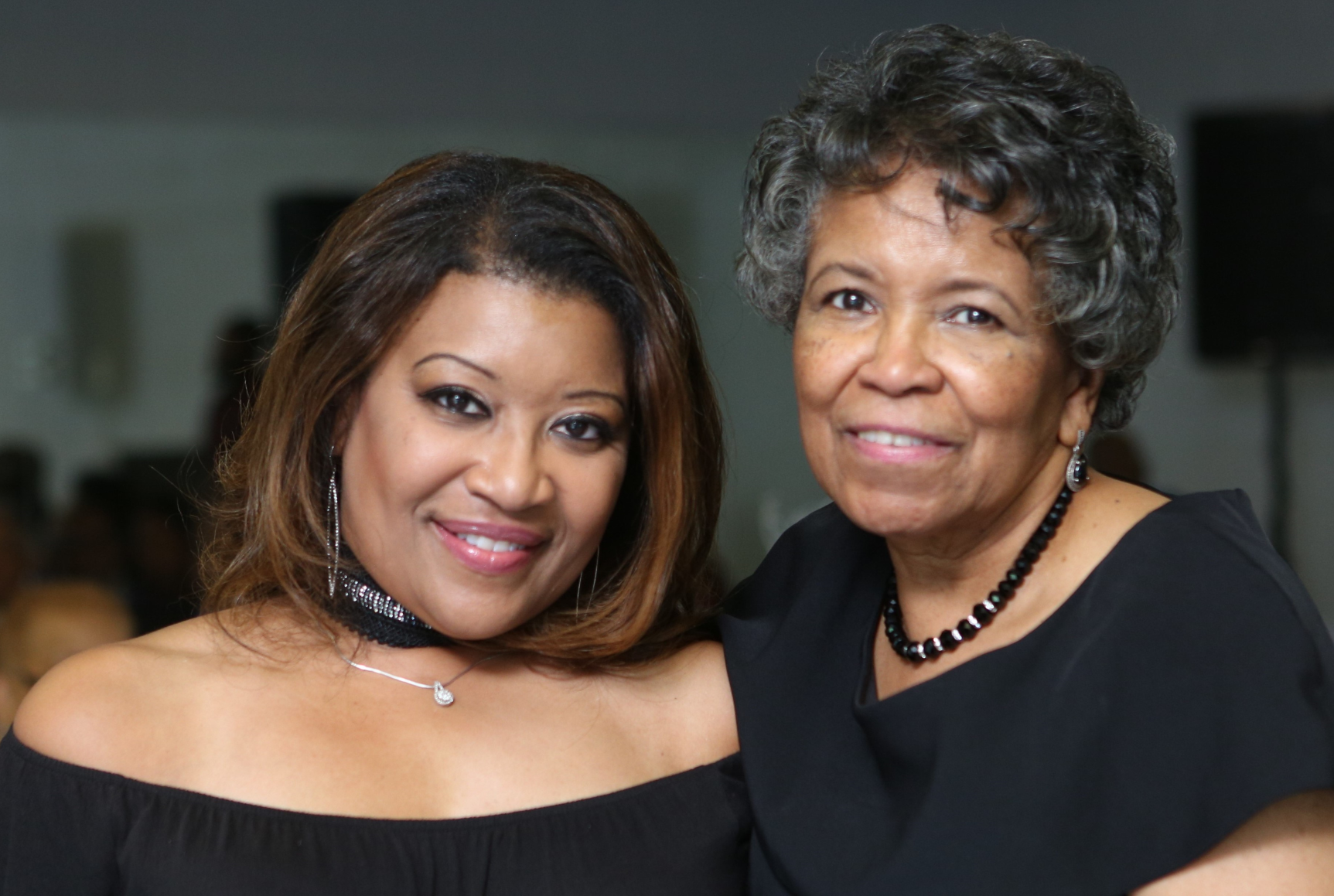 Sharron and her mother, both wearing black formal attire, smile at the camera