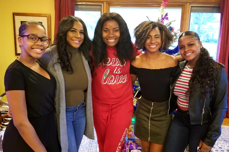 Nikole stands at the center of four women smiling at the camera in front of a Christmas tree